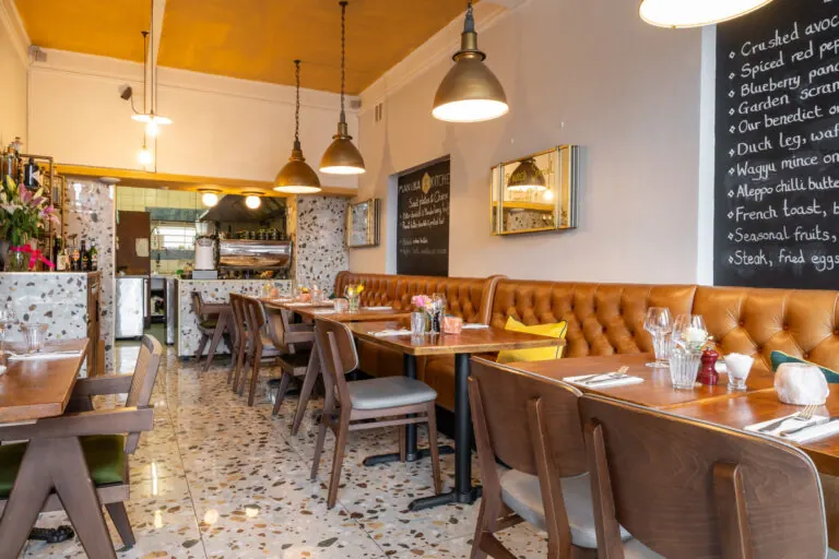 Tan buttoned leather banquettes and wooden tables on a terrazzo floor inside Manuka Kitchen